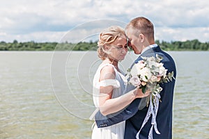 Young blonde bride and groom dance on pier by lake