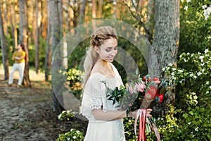 Young blonde bride with a rustic bouquet is posing outdoor in the park. Artwork. Autumn wedding ceremony outdoors.