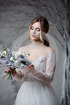 A young blonde bride in white wedding dress on a background of white walls and white tree in the background