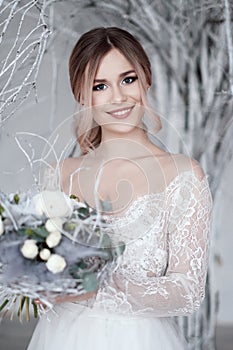 A young blonde bride in white wedding dress on a background of white walls and white tree in the background