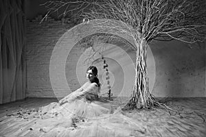 A young blonde bride in white wedding dress on a background of white walls and white tree in the background