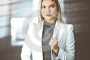 Young blonde business woman or female student standing straight and posing at camera in sunny office