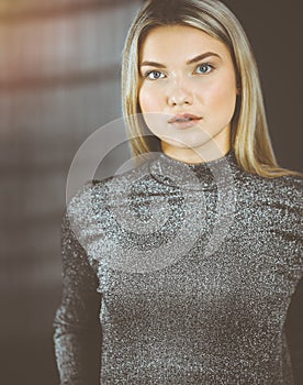 Young blonde business woman or female student standing straight and posing at camera in sunny office