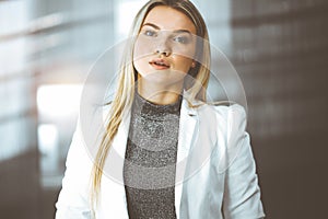 Young blonde business woman or female student standing straight and posing at camera in sunny office