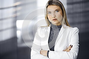 Young blonde business woman or female student in white blazer is standing straight and posing at camera. Lifestyle and