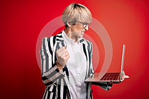 Young blonde business woman with short hair wearing glasses working using computer laptop annoyed and frustrated shouting with