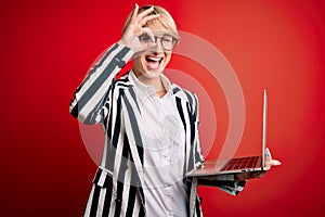 Young blonde business woman with short hair wearing glasses working using computer laptop with happy face smiling doing ok sign