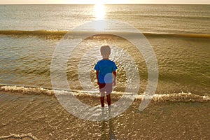 Young boy looking out to a golden sunset reflecting in the ocean