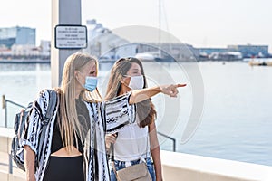 Young blonde caucasian woman pointing with her finger something to an indian friend on a port