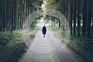 Young blonde caucasian woman walking on road through dark forest