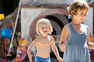Young blonde child girl with friend or sister playing with soap bubbles. Warm sunset light. Family summer trave