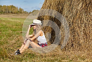 Young blonde country girl in hat near haystack