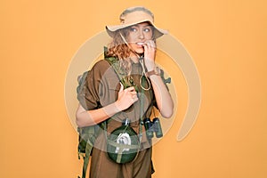 Young blonde explorer woman with blue eyes hiking wearing backpack and water canteen looking stressed and nervous with hands on