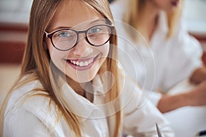 Young blonde female child with cute smile choosing best eyeglass in office ophthalmologist