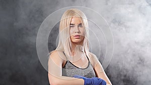 Young blonde female Muay Thai fighter wrapping his hands with blue elastic bandage. Slow motion.