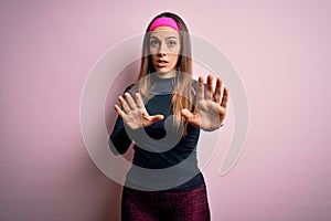 Young blonde fitness woman wearing sport workout clothes over isolated background Moving away hands palms showing refusal and