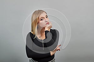 Young blonde girl in black jacket young woman thinks, holds her hand on chin