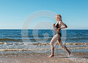 Young blonde girl in a black swimsuit runs along the sand of the sea shore