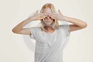 Young blonde girl covering her eyes with hands