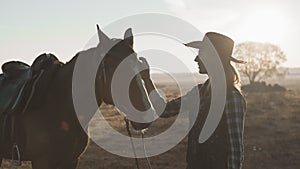 Young blonde girl in cowboy hat stroking and hugging horse and enjoying nature