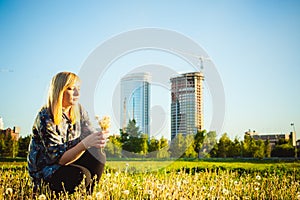 Young blonde girl in dress with shoulder bag, walking on dandelion field