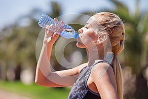 Young blonde girl drinking water during morning jogging