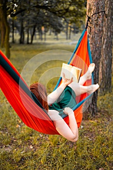 Young blonde girl in hammock reading book. Pretty woman leisure lifestyle at nature ountdoor. Female relax in forest.