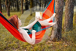 Young blonde girl in hammock reading book. Pretty woman leisure lifestyle at nature ountdoor. Female relax in forest.