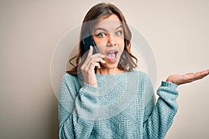 Young blonde girl having a conversation talking on smartphone over isolated background very happy and excited, winner expression