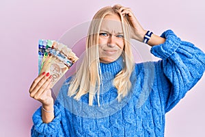 Young blonde girl holding canadian dollars confuse and wondering about question