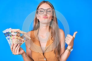 Young blonde girl holding canadian dollars looking at the camera blowing a kiss being lovely and sexy