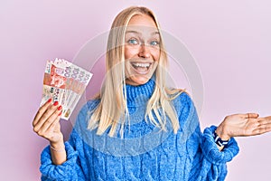 Young blonde girl holding hong kong 10 dollars banknotes celebrating achievement with happy smile and winner expression with