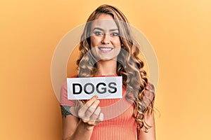 Young blonde girl holding paper with dogs message looking positive and happy standing and smiling with a confident smile showing