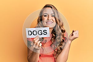 Young blonde girl holding paper with dogs message screaming proud, celebrating victory and success very excited with raised arm