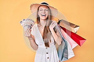Young blonde girl holding shopping bags and mexican pesos banknotes smiling and laughing hard out loud because funny crazy joke