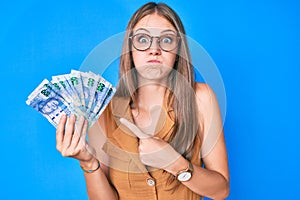 Young blonde girl holding south african rand banknotes puffing cheeks with funny face