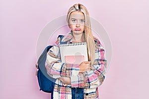 Young blonde girl holding student backpack and books depressed and worry for distress, crying angry and afraid