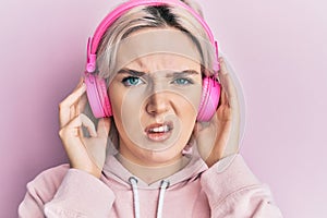 Young blonde girl listening to music using headphones clueless and confused expression