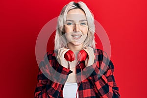 Young blonde girl listening to music using headphones smiling with a happy and cool smile on face