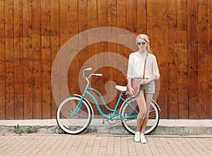 Young blonde girl with long hair in green sunglasses standing near vintage green bicycle have fun and good mood looking in ca
