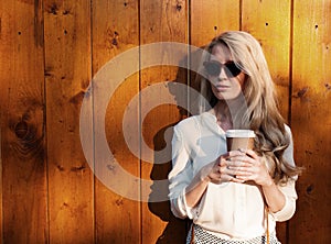 Young blonde girl with long hair in sunglasses holding a cup of coffee have fun evening soft sunlight, warm, tonning