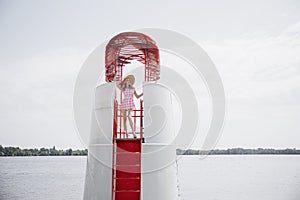 Young blonde girl look like a Barbie doll in pink mini dress and wide brim hat standing on lifeguard beach tower