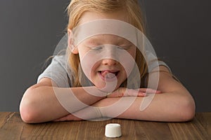 A young blonde girl looks at a single marshmallow