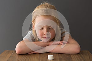 A young blonde girl looks at a single marshmallow