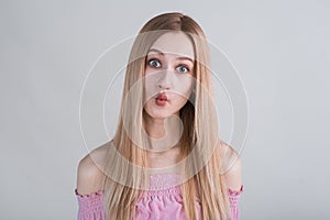 Young blonde girl makes funny grimaces in the studio on a white background.