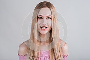 Young blonde girl makes funny grimaces in the studio on a white background.