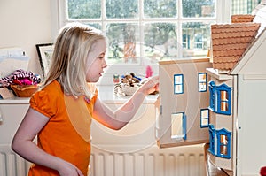 A young blonde girl opens a dolls house and looks inside