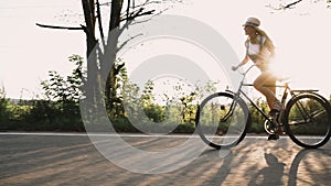A young blonde girl in pants on retro bike going down the road in the field