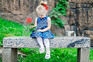 Young blonde girl in the park sits on a bench with a rose