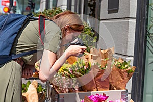 Young girl photographer makes a photo of assorted flowers bouquets in a shop on the street